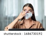 Don't Touch Your Face. Girl wearing surgical mask rubbing her eye with dirty hands, working on laptop