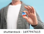 Small photo of Vote 2020 in America, US. Law abiding american citizen holding vote pin in hand, blurred background