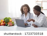 Small photo of African women dietician and patient looking at laptop screen at dietologist cabinet, copy space