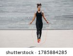 Female athlete does cardio workout. Smiling african american girl in sportswear with fitness tracker jumping rope outdoors, free space