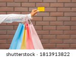 Modern payment for purchases. Female hand with shopping bags gives credit card to seller on brick wall background, copy space, cropped