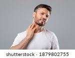 Small photo of Middle aged bearded man scratching highlighted with red neck on grey studio background, copy space. Annoyed man suffering from itch, having rash on his neck. Allergic reaction, eczema concept