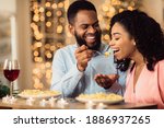 Romantic Relationship. Beautiful young african american couple in love sitting in cafe and eating dinner. Smiling man is feeding his woman with pasta. Glasses with red wine and candles on the table