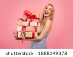 Excited pretty blonde lady in dress holding stack of gift boxes over pink studio background. Celebrating Woman's Day, Valentine's, birthday, anniversary. Shopping for holiday concept