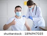 Small photo of Get vaccinated. Young Caucasian guy showing thumbs up during coronavirus vaccination at clinic, promoting covid-19 immunization. Protection against global virus concept