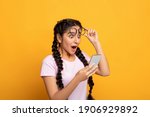 Wow, Great News. Portrait Of Excited Surprised Indian Woman Holding And Using Smartphone, Browsing Social Media. Emotional Young Lady Having Success, Taking Off Glasses, Yellow Studio Background