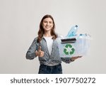 Small photo of Positive Eco-Friendly Woman Holding Container With Plastic Bottles And Showing Thumb Up Gesture, Smiling Millennial Female Agitating For Waste Sorting And Recycling Over Gray Studio Background