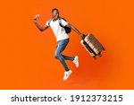 Small photo of Bye-bye, Im going vacation. Young happy black man with suitcase, backpack, passport and flight tickets jumping up orange studio background. Excited african american guy running and looking back