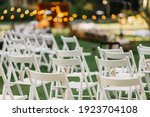 Modern stylish outdoor wedding, catering and design of rite. A lot of white folding chairs with paper packages with petals on green lawn for marriage ceremony in summer, flat lay, nobody, free space