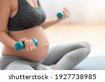 Cropped Shot Of Unrecognizable Pregnant Woman Training With Dumbbells At Home, Expectant Lady In Sportswear Exercising On Fitness Mat In Living Room, Closeup Image With Free Space