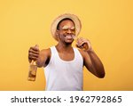 Positive black guy in summer outfit holding two bottles of beer, drinking alcoholic beverage on yellow studio background. Cheerful African American man advertising your brewery, having party
