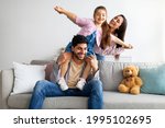 Cheerful young eastern parents having fun with child in living room, playing and laughing, enjoying spending time together. Happy arab family with daughter at home