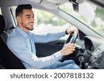 Handsome middle-eastern businessman driving car, going on business trip, side view, copy space. Happy arab man in stylish outfit going to business meeting or to office, driving his luxury car