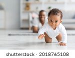 Adorable Black Infant Baby Crawling Away From Father While Resting Together In Living Room At Home, Cute Little African American Toddler Child Playing With Daddy, Selective Focus, Copy Space