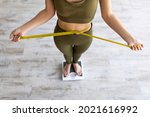 Unrecognizable Indian female measuring waist while standing on scales, checking weight loss result, measuring body parameters after slimming diet at home, above view