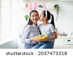 Holiday and celebration concept. Cute asian girl and woman wearing rabbit bunny ears on Easter day, copy space. Pretty kid kissing mom in cheek and holding basket full of painted eggs