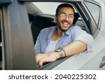 Cheerful arab guy passenger sitting at auto back seat, looking through window and smiling, enjoying car ride, closeup portrait. Happy indian man taking taxi, going to office, copy space