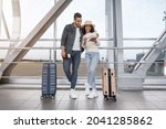 Small photo of Waiting For Flight. Happy Arab Couple Standing At Airport Terminal With Suitcases, Excited Middle Eastern Spouses Checking Passports And Tickets While Standing With Luggage Near Window, Copy Space