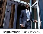 Young african american entrepreneur man leaving business center building after work, looking away and smiling, copy space. Business people and successful career concept