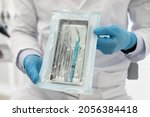 Small photo of Doctor Wearing Blue Sterile Gloves Demonstating Sealed Sterilization Pouch With Clean Dental Tools, Unrecognizable Male Dentist Showing Stomatological Instruments, Ready For Teeth Treatment, Closeup