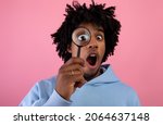 Small photo of Shocked black teen guy looking through magnifying glass on pink studio background. Surprised African American teenager suspecting, investigating or questioning something. Secret, doubt concept