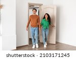Small photo of Smiling couple opening door and walking in their apartment, entering new home, happy cheerful young guy and lady standing in doorway of modern flat, looking at design interior together, coming inside