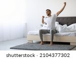 Good Morning. Happy Millennial Arab Guy Sitting On Bed And Stretching After Good Sleep, Handsome Smiling Young Middle Eastern Man Relaxing In Cozy Bedroom, Enjoying Home Comfort, Copy Space