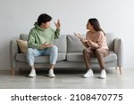 Small photo of Breakup and divorce concept. Young married Asian couple having fight, yelling at each other in living room. Furious man and woman shouting at one another, sitting on sofa at home