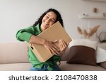 Shopping And Delivery. Contented Woman Buyer Hugging Cardboard Box Sitting On Couch At Home. Female Customer Being Happy About Delivered Package From Shop. Shopaholism And Commerce Concept