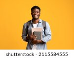 Positive african american millennia guy student in casual posing with books and notepads on yellow studio background, young black man enjoying studying at university or college, copy space