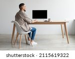 Rear Back View Of Happy Smiling Arab Man Looking At Pc Computer With Blank Black Screen For Mock Up Template Sitting At Desk At Home Office, Free Copy Space. People, Technology, Remote Work Concept