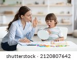 Speech therapy concept. Cute little boy pronouncing sound O looking at mirror, professional woman therapist teaching kid right pronounciation during private lessong at office