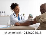 Small photo of Vaccination, Immunization, Disease Prevention Concept. Mature black man getting Covid-19 or flu vaccine at the hospital. Professional female doctor giving antiviral jab to elderly citizen