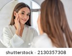 Small photo of Natural Beauty. Portrait Of Attractive Young Female Smiling To Her Reflection In Mirror, Beautiful Millennial Woman Enjoying Her Appearance While Getting Ready In Bathroom, Selective Focus