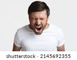 Small photo of Anger. Mad Male Shouting Loudly In Anger With Eyes Closed Expressing Fury Posing Standing On White Background. Rage, Negative Emotions Concept. Studio Shot