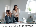 Small photo of Displeased female boss scolding upset subordinate, pointing at mistake in business project at office. Male worker using pc, missing deadline, speaking to unhappy colleage, feeling stressed at work