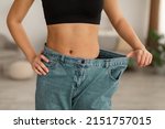 Successful Weight Loss. Unrecognizable Skinny African American Woman Wearing Old Large Jeans After Showing Flat Belly And Great Result After Slimming Standing At Home. Cropped Shot