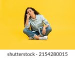 Small photo of Portrait of tired young woman leaning head on hand fist, bored indifferent female feeling exhausted and sleepy sitting on the floor isolated over yellow orange studio background wall