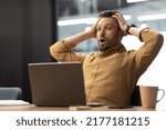 Small photo of Business Problem. Shocked Male Entrepreneur Looking At Laptop In Shock Touching Head Reading Awful News Online Sitting In Office Indoors. Entrepreneurship Issues Concept