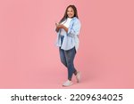 Black Plus Size Woman Using Smartphone Standing On Pink Studio Background, Smiling To Camera. Cheerful Female Using New Mobile Application And Texting. Technology And Gadgets. Full Length
