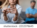 Unhappy middle aged european lady takes off ring, ignoring man during quarrel in living room interior, cropped. Relationship problems, divorce, scandal and breakup, emotions at home due covid-19