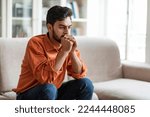 Small photo of Permacrisis, life problems, financial hangout concept. Pensive young middle eastern man sitting on sofa at home, leaning on his hands, experiencing difficulties in life, looking at copy space