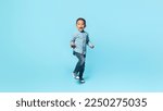 Yes. Happy little black kid boy shaking fists, making winner gesture, celebrating victory and win, standing over blue studio background wall, panorama