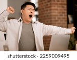Tired bored middle aged asian man yawning while sitting at workplace with computer, wants to sleep at home interior. Work and business with modern technology, fatigue and overwork, deadline
