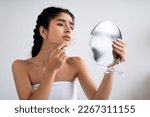 Small photo of Worried Indian Female Holding Magnifying Mirror And Looking At Pimple On Her Chin, Upset Young Beautiful Hindu Female Making Daily Beauty Care, Suffering Acne On Face, Having Problem Skin, Closeup