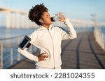 Small photo of Young african american woman drinking water, having break during training outdoors, thirsty black female enjoying refreshing drink after jogging, wearing wireless earphones and armband, copy space
