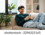 Small photo of Great Mobile Offer. Cheerful Arabic Man Using Phone Lying On Couch Relaxing At Home On Weekend. Guy Using New Application On Smartphone, Browsing Internet And Texting Online. Gadgets Lifestyle