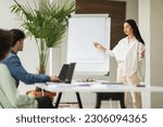 Small photo of Corporate Presentation. Successful Japanese Businesswoman Presenting Her Project Ideas Pointing At Whiteboard Standing In Modern Office During Coworkers Meeting. Business Storytelling Skills