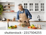 Small photo of Smiling senior man cooking fresh vegetable salad in kitchen, adding olive oil and seasoning to bowl, elderly gentleman wearing apron making healthy vegetarian food at home, copy space
