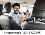 Small photo of Cheerful arab man holding key from auto, buying brand new car in showroom. Happy middle eastern guy buying new automobile, sitting inside car, showing automatic key at camera, gesturing